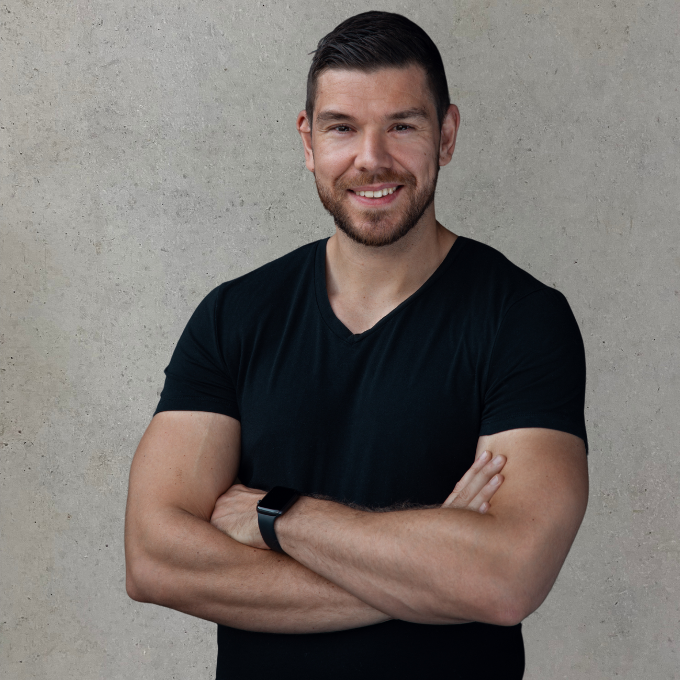 Christian Mann mit breitem Lächeln und verschränkten Armen, trägt ein schwarzes T-Shirt.