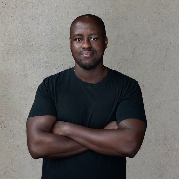 Onya Mann mit verschränkten Armen, trägt ein schwarzes T-Shirt, mit neutralem Hintergrund.